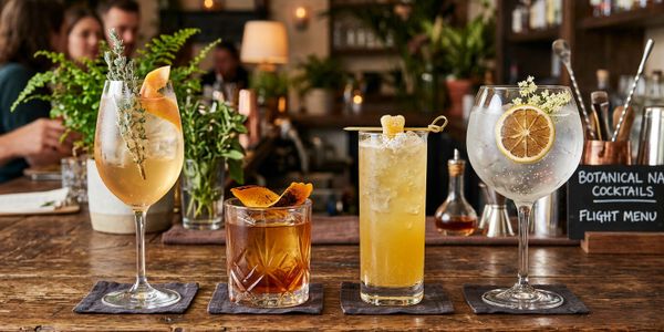 Four elegant cocktails lined up on a wooden bar counter with a cozy background.