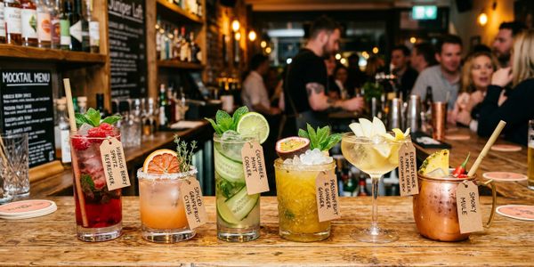 Colorful mocktails lined up on a wooden bar counter with tags.