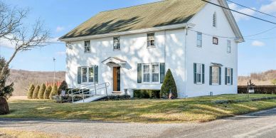 White two-story house with green shutters and a ramp at the entrance.