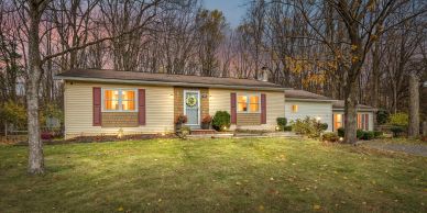 Cozy single-story house with warm lights and autumn trees at dusk.