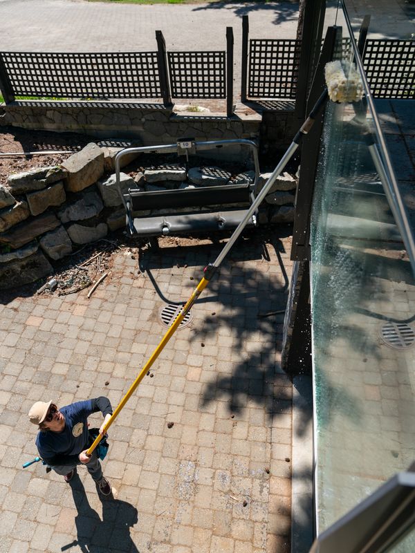 Cleaning the glass railing of a patio with an eco-friendly solution, pole and a squeegee in Squamish