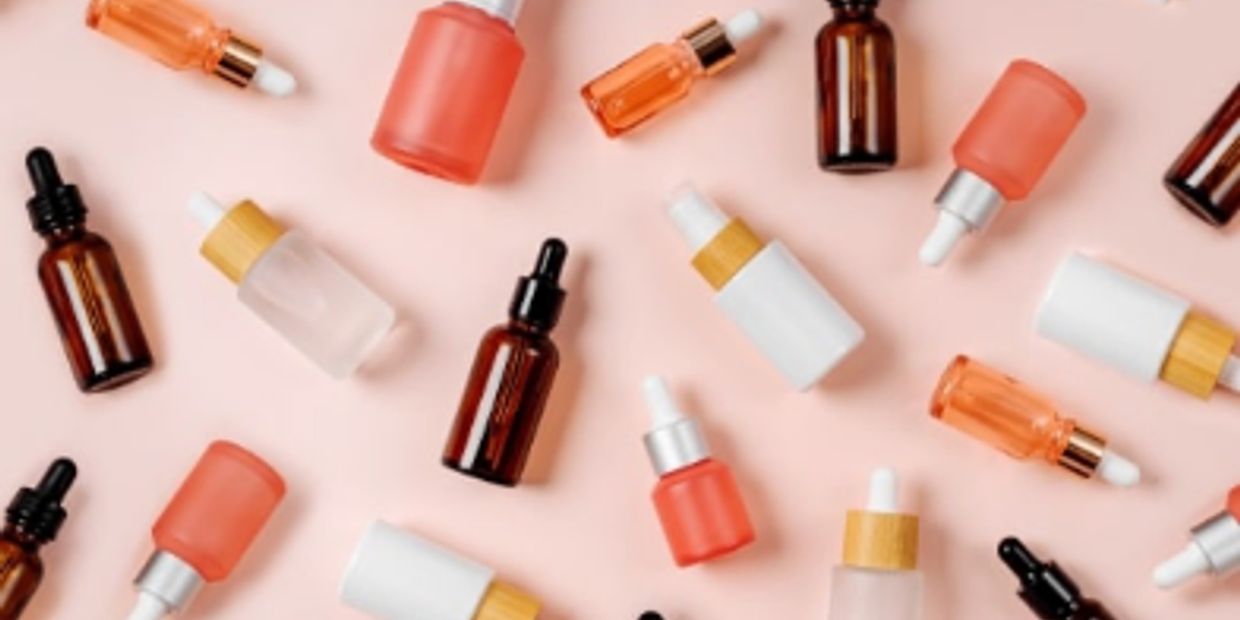 Various cosmetic dropper bottles arranged on a light pink surface.