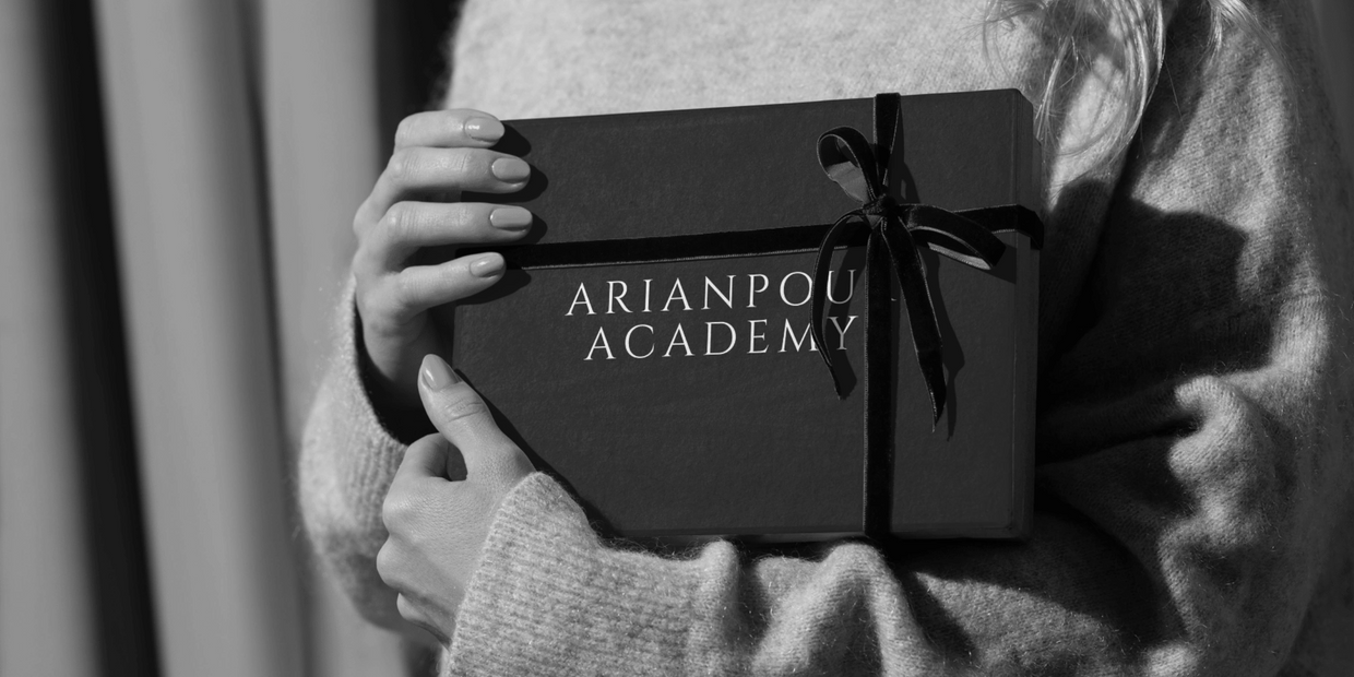 Person holding a gift box wrapped with a ribbon labeled Arianpour Academy.