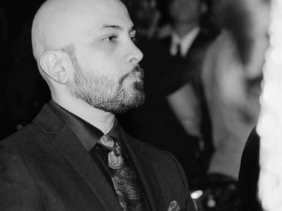 Profile of a bald man in a suit with a red pocket square.