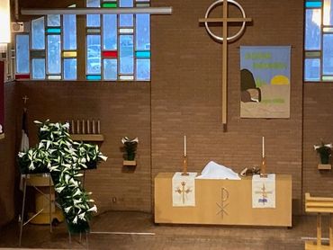Interior of a church altar with a cross and decorated with lilies.