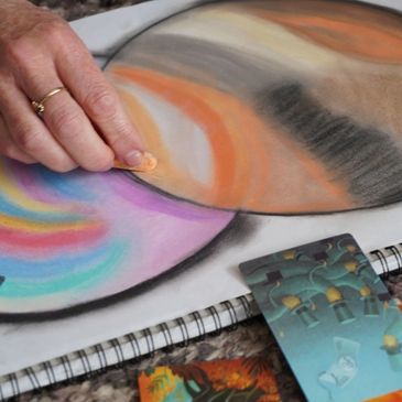Hand blending vibrant pastel colors on paper with a finger.