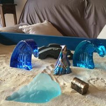 A miniature wizard figurine surrounded by glass waves and a treasure chest.
