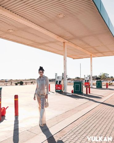 Woman walking at an empty gas station in bright sunlight.