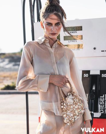 Fashion model with sheer outfit and floral bag at gas station.
