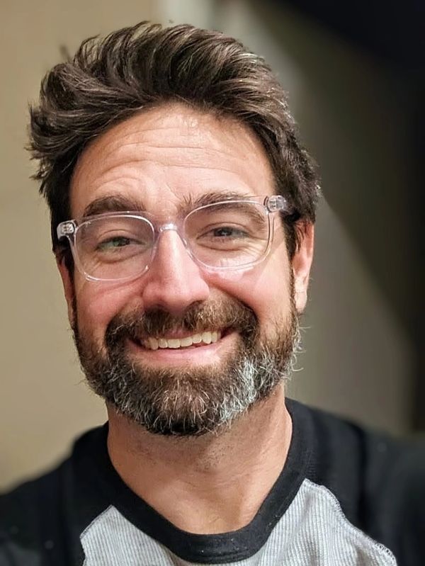 Smiling man with glasses and a beard wearing a casual shirt.