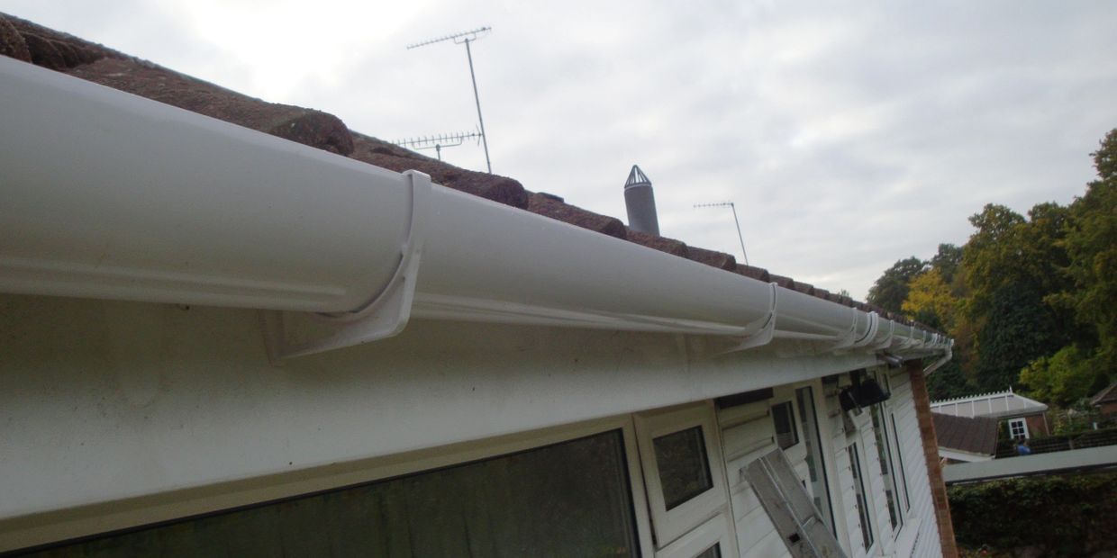 White gutter system attached to a house roof under a cloudy sky.