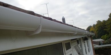 White rain gutter attached to the edge of a house roof under a cloudy sky.