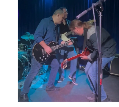 Three musicians passionately playing guitars on stage during a live performance.