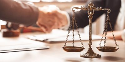 Handshake behind a justice scale symbolizing agreement and fairness.