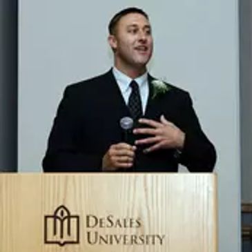 Man speaking at a podium with DeSales University logo.