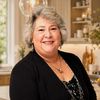 Smiling elderly woman with gray hair in a cozy home setting.
