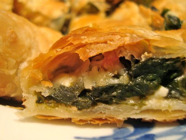 Close-up of a spinach and cheese filled pastry with flaky crust.