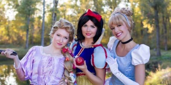 Two girls wearing tiaras celebrating a birthday with cupcakes and candles.