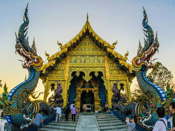 Golden temple entrance guarded by intricate dragon sculptures with visitors ascending steps.