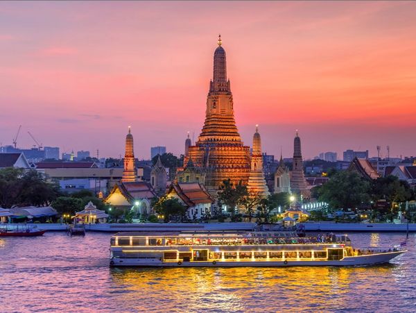 Wat Arun temple illuminated at sunset with a boat on the river in Bangkok.