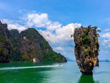 Unique tall rock formation in clear green water with mountain backdrop.