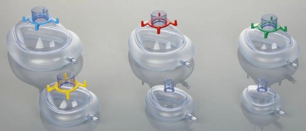 Various transparent anesthesia masks with colored connectors arranged on a reflective surface.