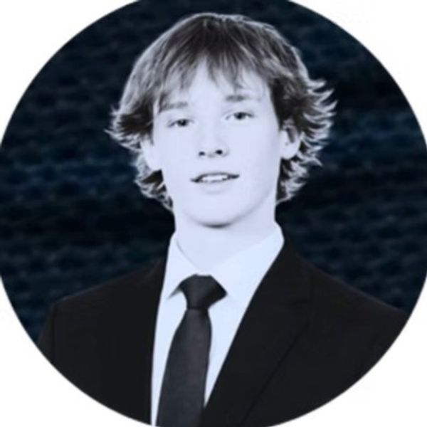Young man in a formal suit and tie with a blurred dark background.