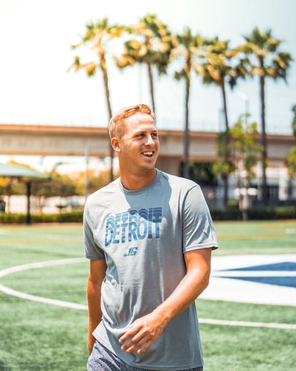 Young man smiling on a sunny sports field with palm trees.