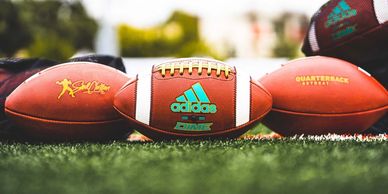 Three footballs on grass, one with Adidas logo.