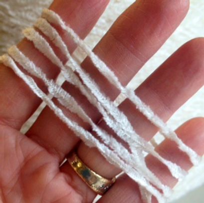 Hand holding several strands of white yarn with spaced knots.