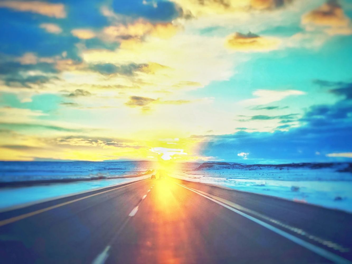Sunset glowing on an open highway with snowy surroundings.