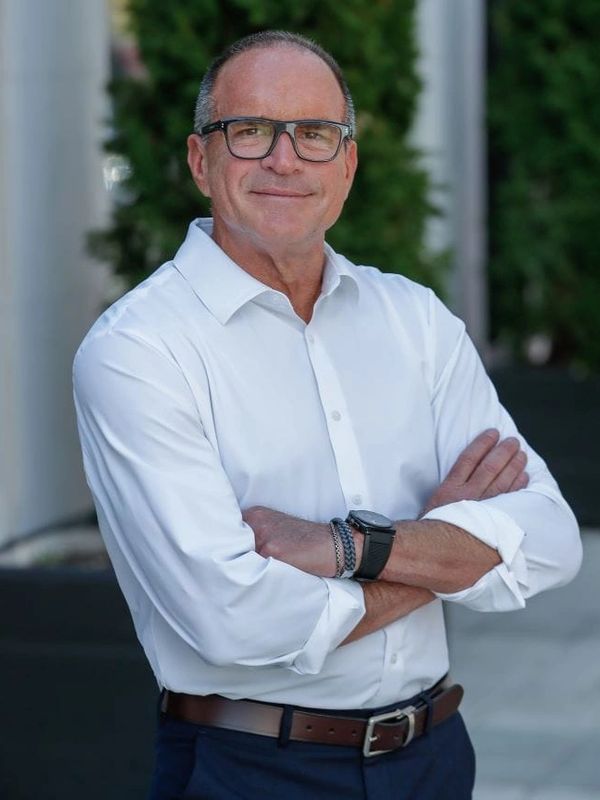 Confident man in glasses wearing a white shirt with arms crossed outdoors.