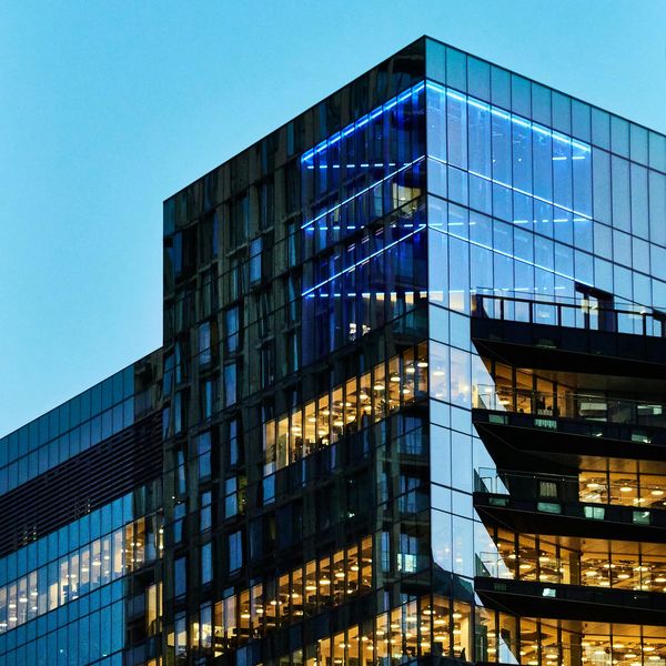 Modern glass building illuminated with blue and yellow lights at dusk.