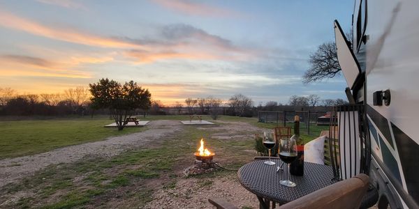 Image of the sitting area in front of the River RV with fire pit burning and glasses of wine on the 