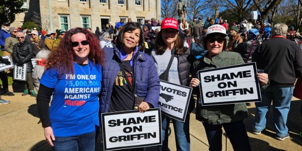 Four women at a public protest holding signs against Griffin.