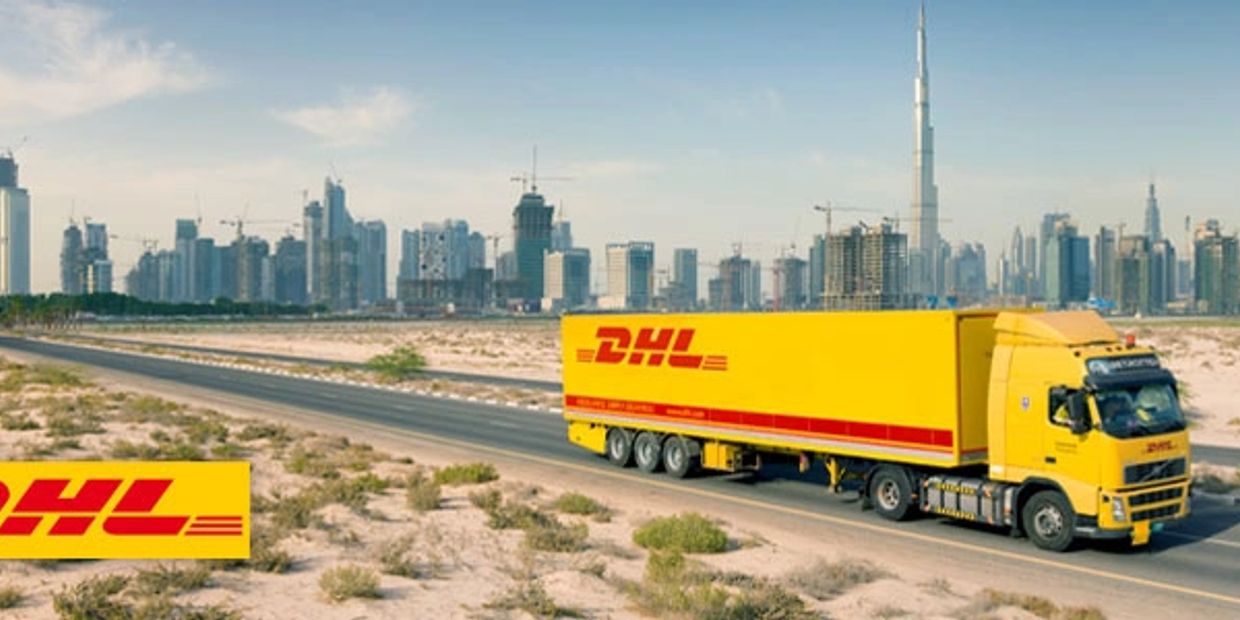 DHL truck driving on a desert road with a city skyline in the background.
