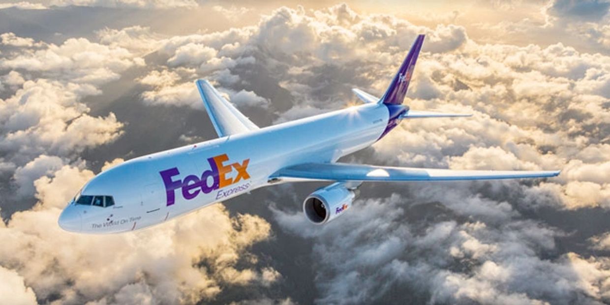 FedEx airplane flying above clouds during sunset.