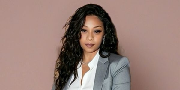 Confident woman in a gray blazer and white shirt against a beige backdrop.