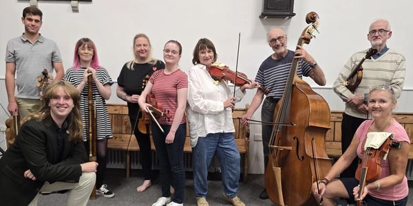 A group of nine musicians posing with their string instruments indoors.