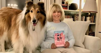 Smiling woman with a collie dog holding a book on a cozy couch.