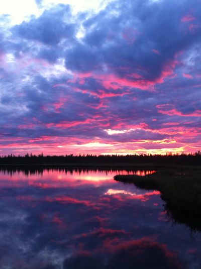 Reflection of a lake at dusk in the ​​Sǫ̀mba K’è area, dark shoreline and sunset breaks the skyline.