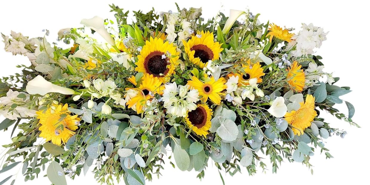 A coffin spray filled with bright yellow sunflowers and gerberas, calla lilies and eucalyptus