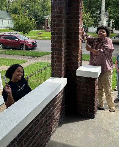 Two people painting a brick porch white.