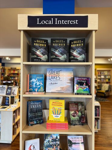 Books on local interest topics displayed on a wooden shelf in a bookstore.
