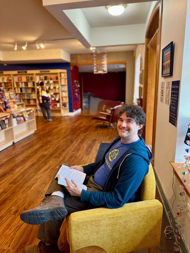 Man sitting on a yellow chair reading a book inside a bookstore.
