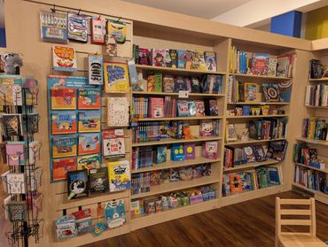 Children's books and educational supplies neatly displayed on wooden shelves in a cozy bookstore.