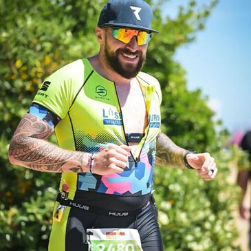 Smiling athlete running outdoors in vibrant triathlon gear and sunglasses.