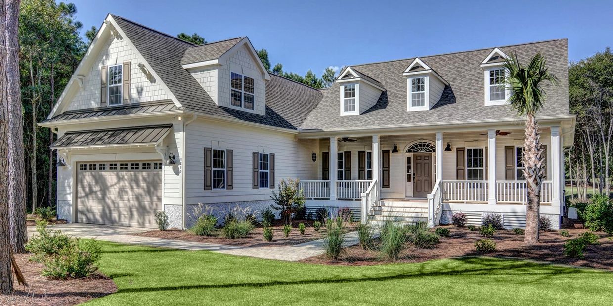 A modern cottage-style home with white exterior, dormer windows, and a front porch with columns.