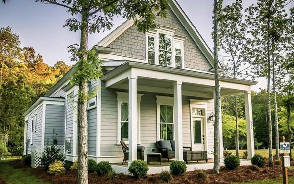A quaint two-story home with gray siding and white trim, featuring a covered porch.