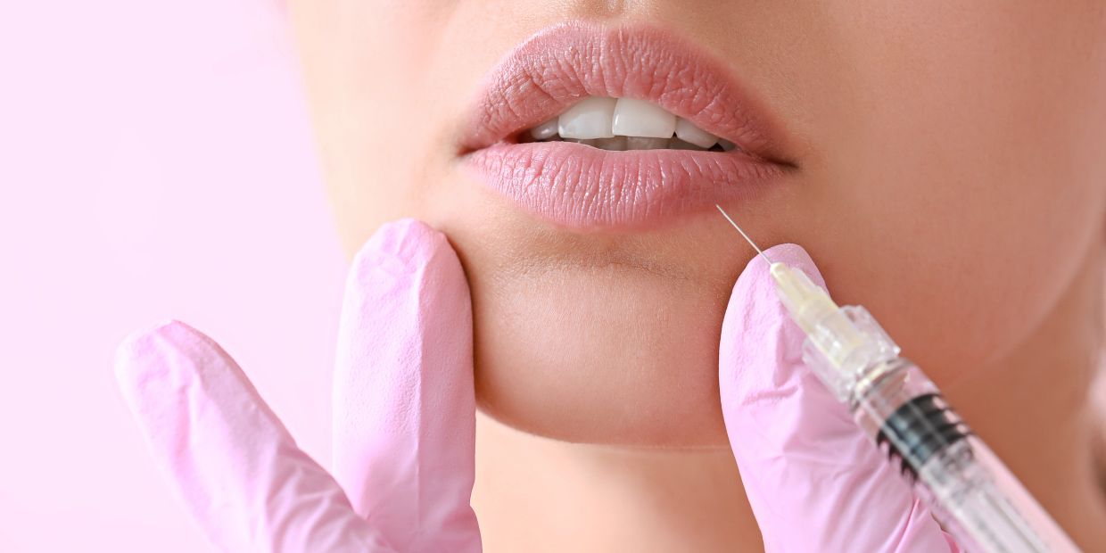 Close-up of lip injection procedure with pink gloves and syringe.